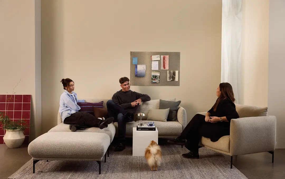 Drei Personen auf hellem Sofa mit Hocker und kleinem Hund auf Teppich im Wohnzimmer